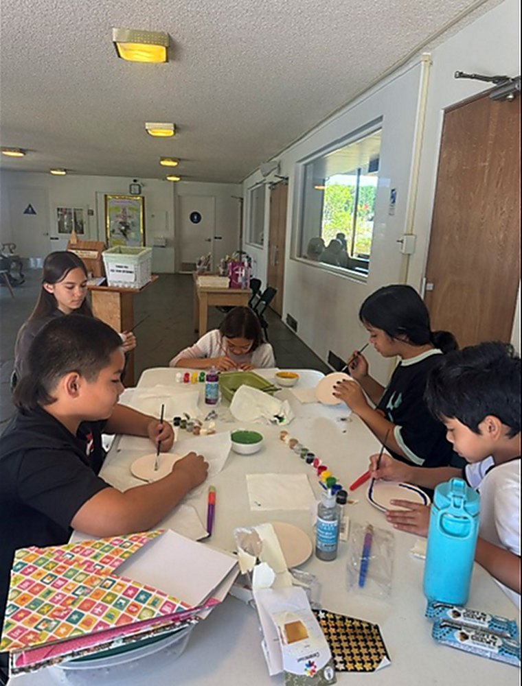 Children seated around a table painting ceramic crafts in the fellowship hall