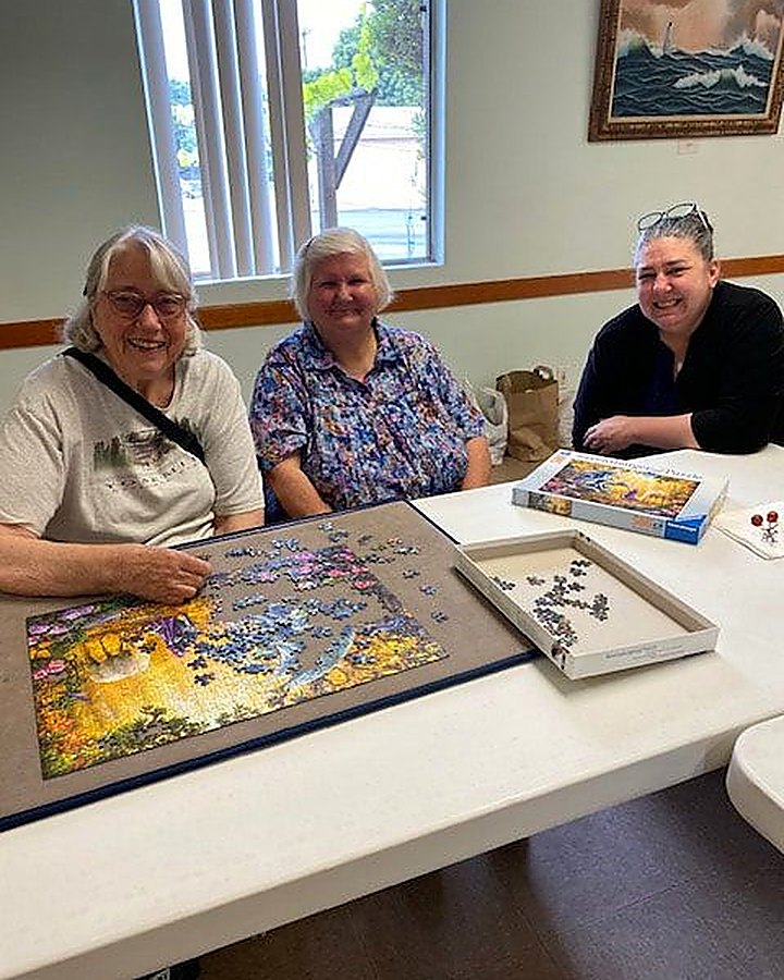 Three members of the Craft n Craic group working on a jigsaw puzzle together at a table