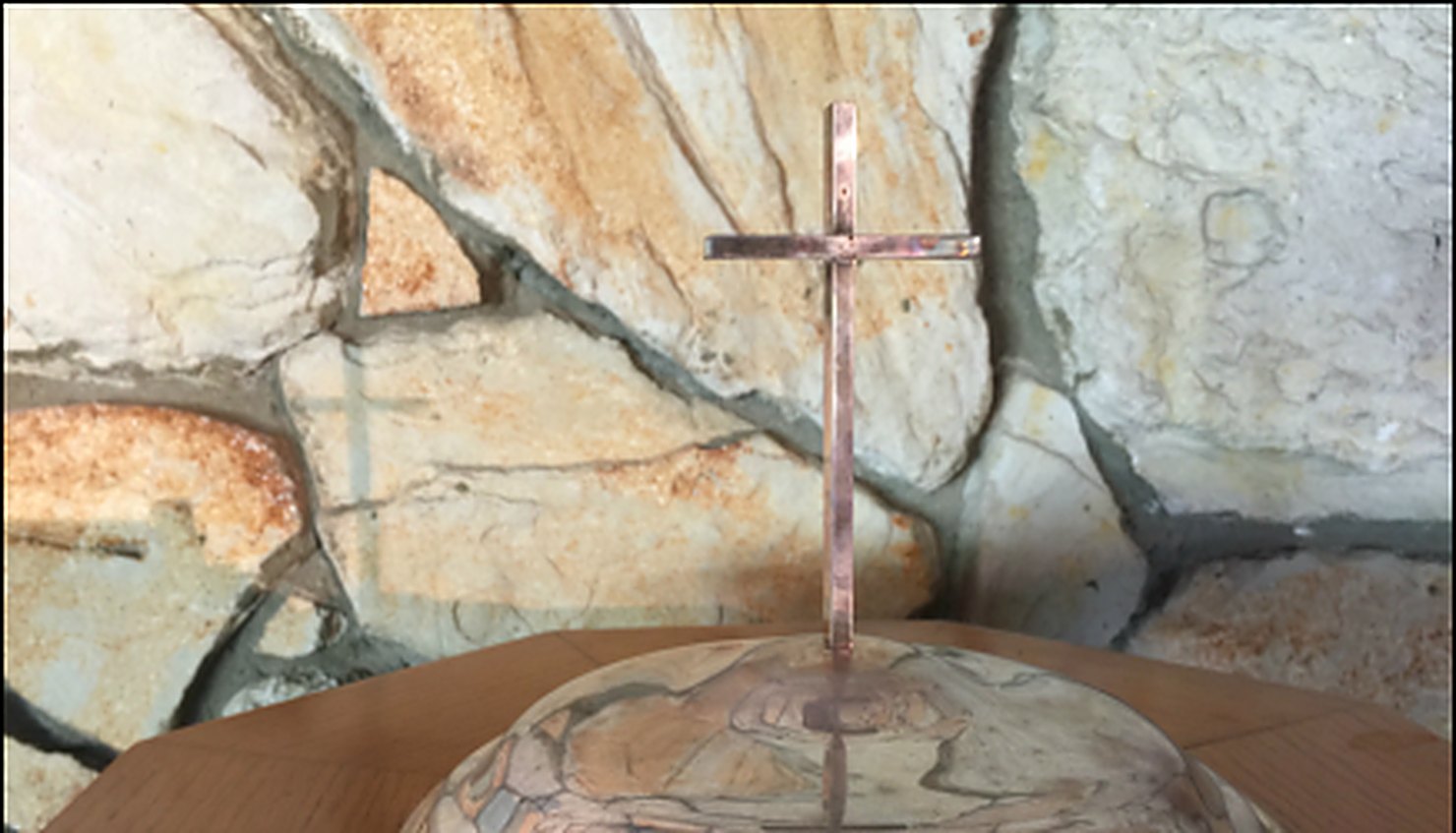 The stone wall of the St. Mark's sanctuary with a standing brass cross