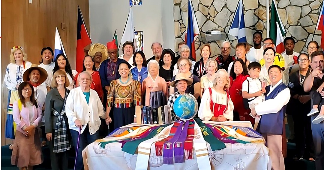 The congregation of St. Mark's gathered in the sanctuary, many in traditional dress, with the flags of many nations behind them